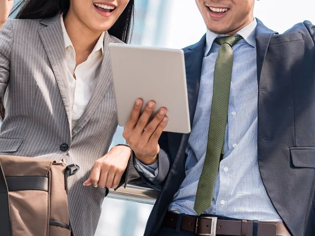 A man and a woman standing behind and looking at a tablet.
